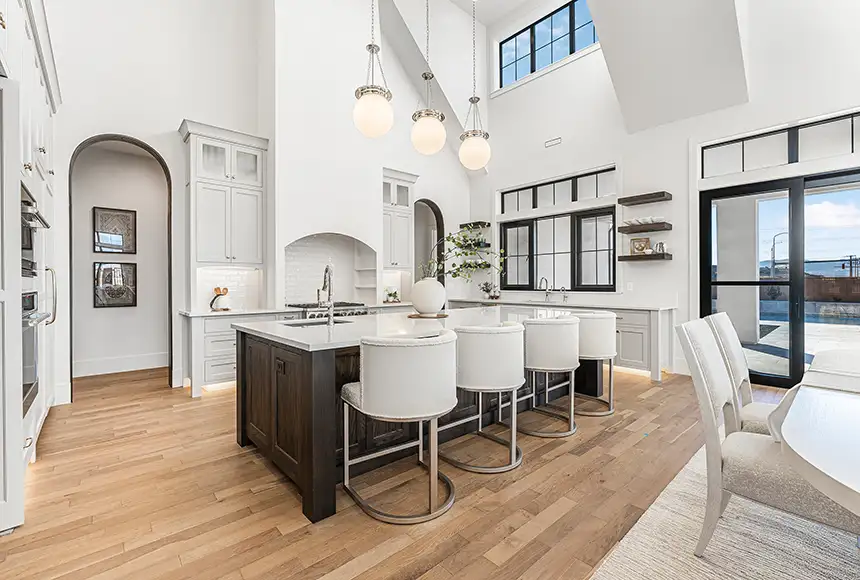 Bright white kitchen with a dark wood island, white bar stools, and globe pendant lights