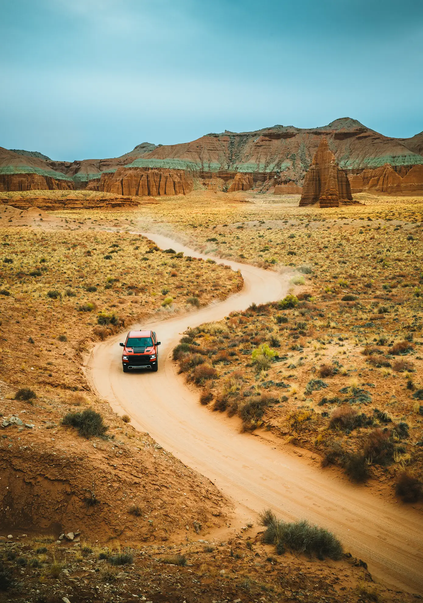 Red pickup truck driving a winding dirt road through a red rock desert