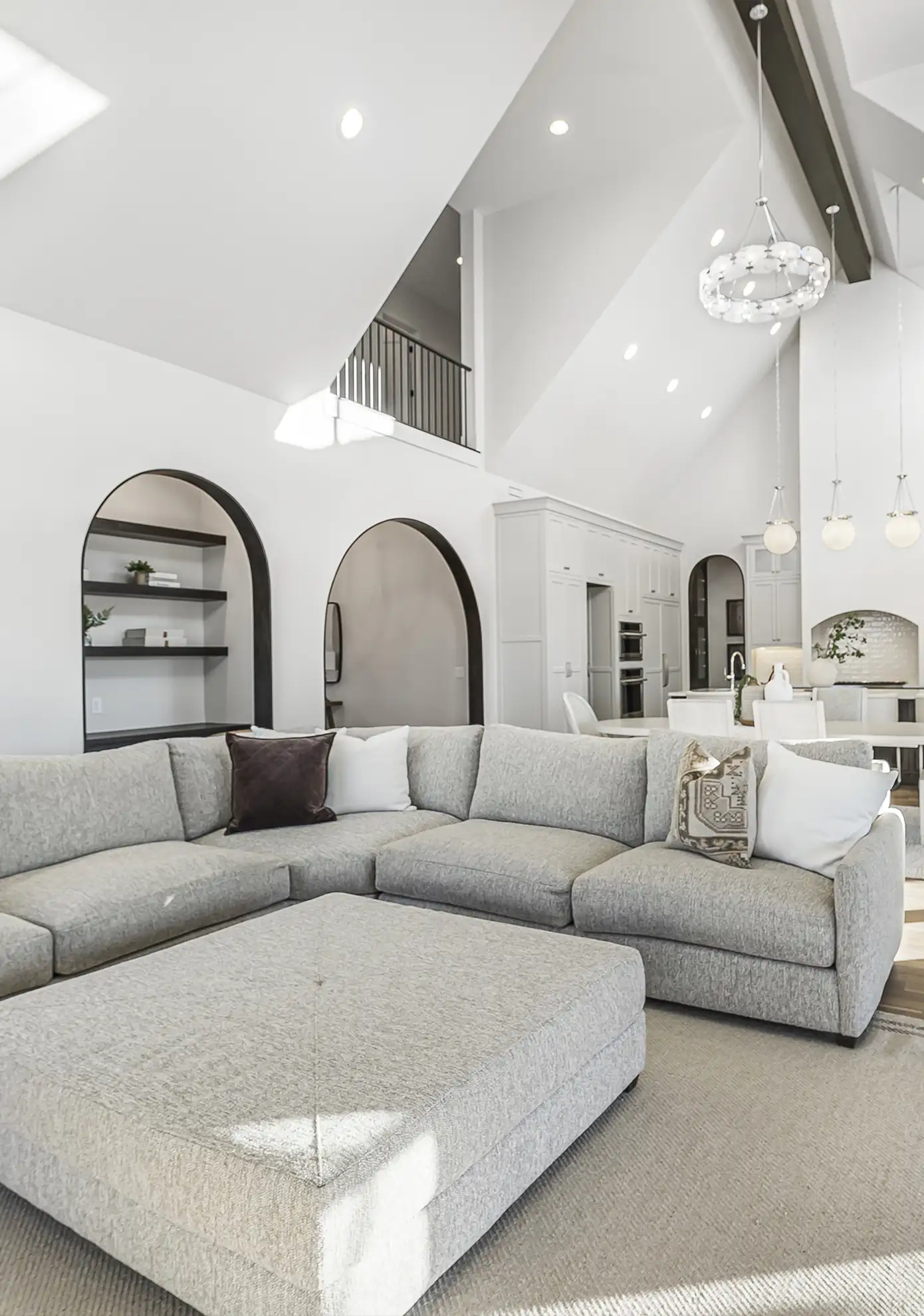 Vaulted great room with a gray sectional, arched built-ins, and an open kitchen beyond