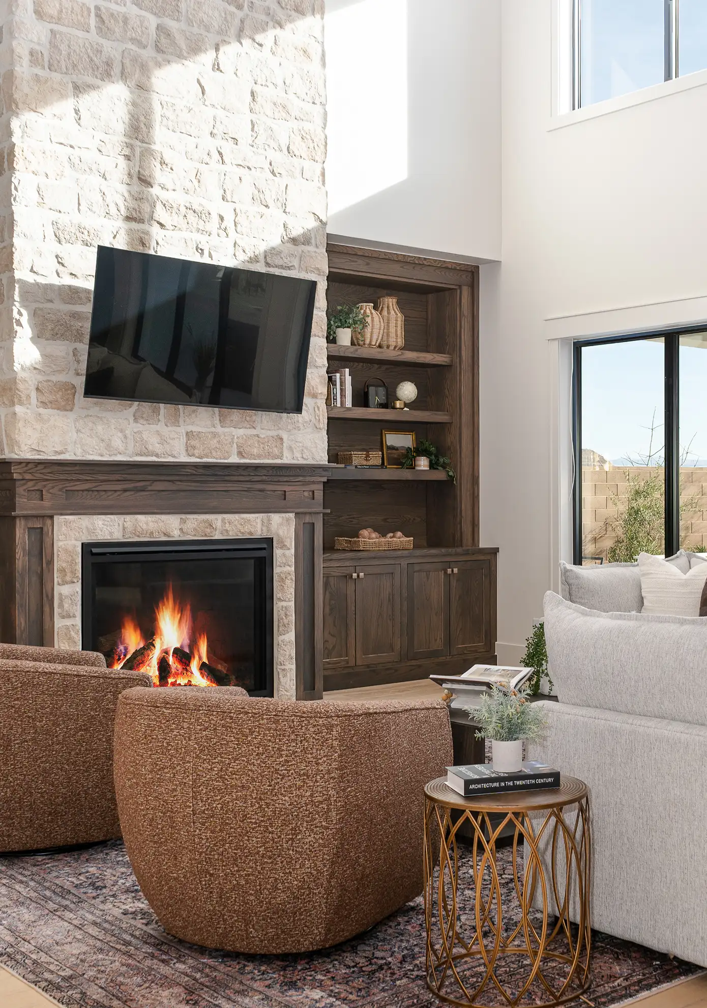 Two-story living room with a stone fireplace, wood built-ins, swivel chairs, and a gray sectional