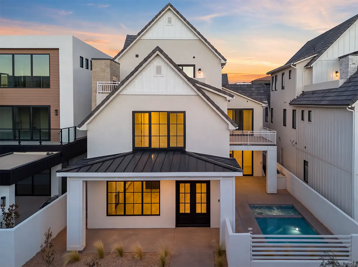 White three-story home with a metal porch roof and a small pool at dusk