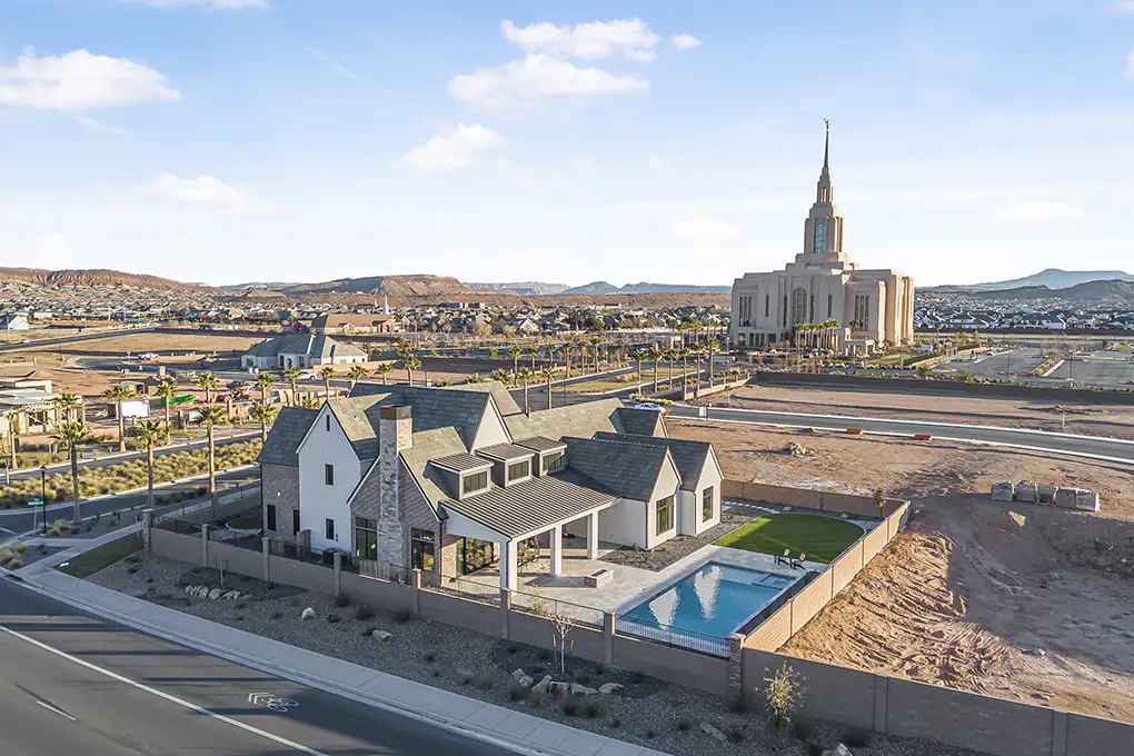 Aerial view of a home with a backyard pool in a desert neighborhood, with a temple in the distance