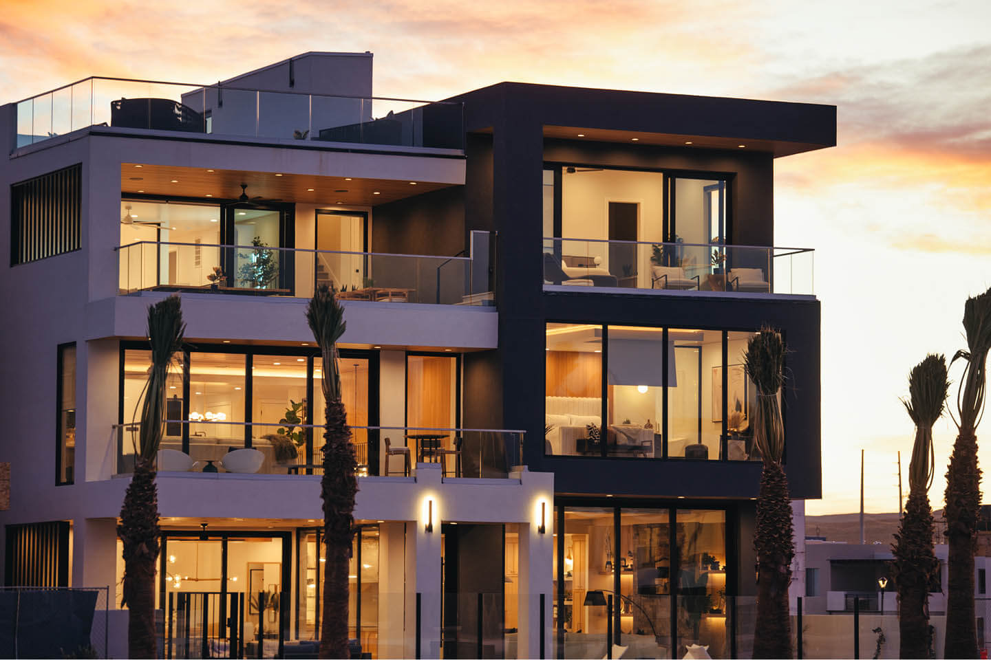 Modern three-story house with large glass windows and balconies at sunset.