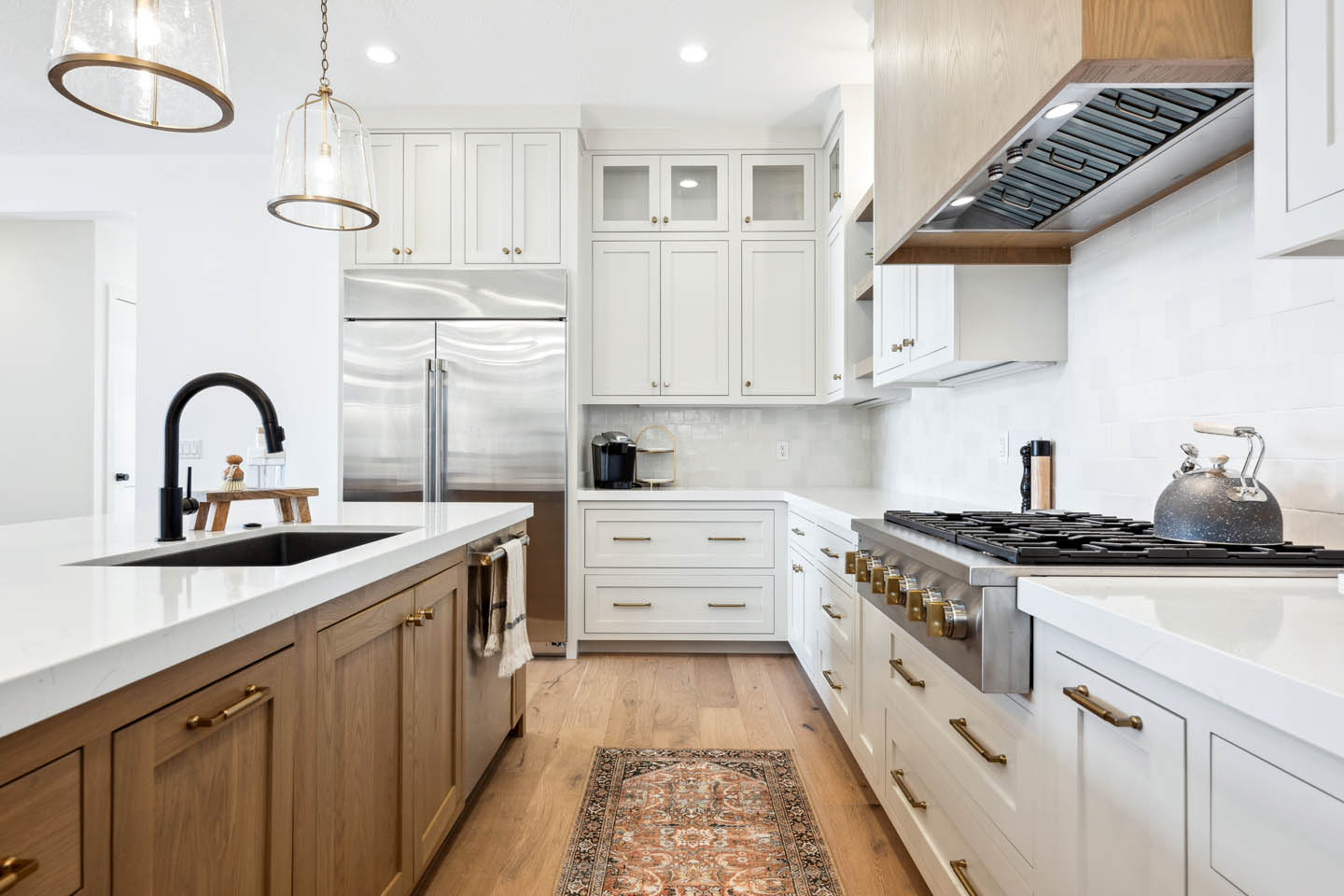Gourmet kitchen with white quartz countertops, shaker cabinetry, natural wood island, brass hardware, glass pendants, professional gas range with wood hood, and dark undermount sink.