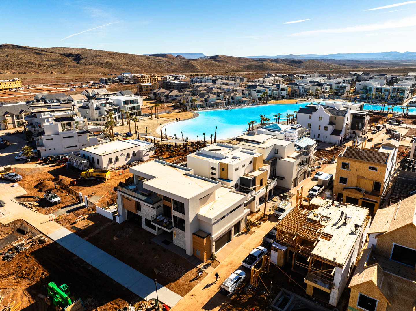 Aerial view of the Desert Sapphire community with modern white and earth-toned homes surrounding a large turquoise lagoon-style pool, set against arid desert hills.
