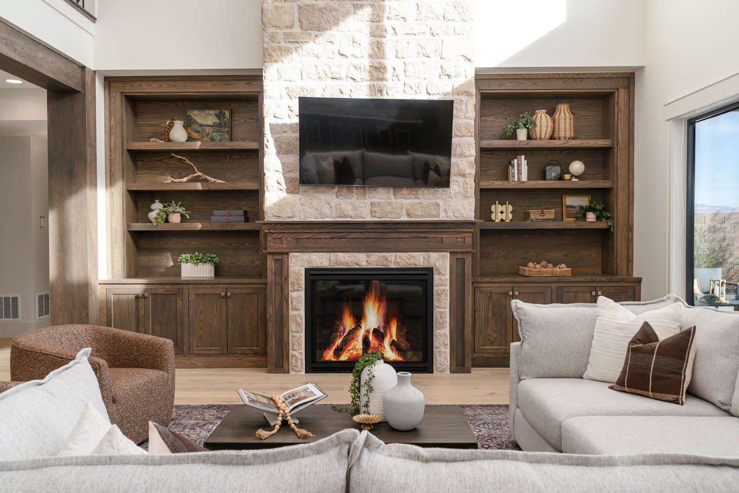Grand living room with stone fireplace, dark wood built-ins, neutral linen sectional, swivel chair, and vintage area rug over light hardwood floors.