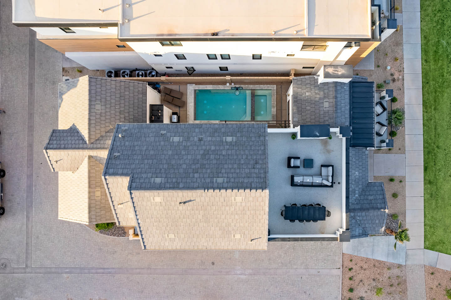 Aerial view of the Sand Cove property showing the roofline, backyard pool surrounded by stone pavers, outdoor dining area, lounge seating, and adjacent green lawn areas.