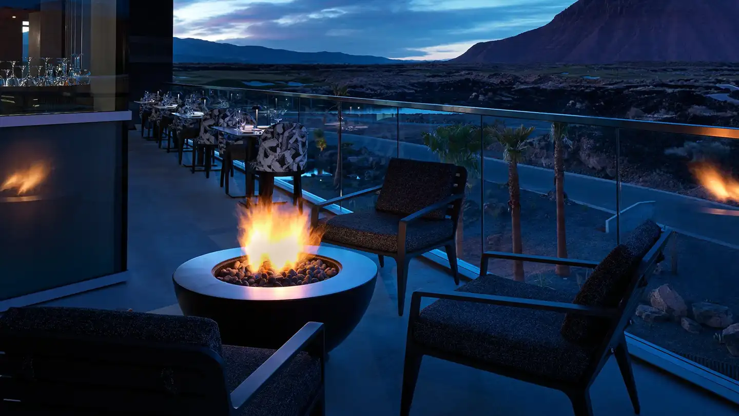 Upscale resort rooftop terrace at dusk featuring a glowing fire bowl, modern lounge chairs, and panoramic desert mountain views.