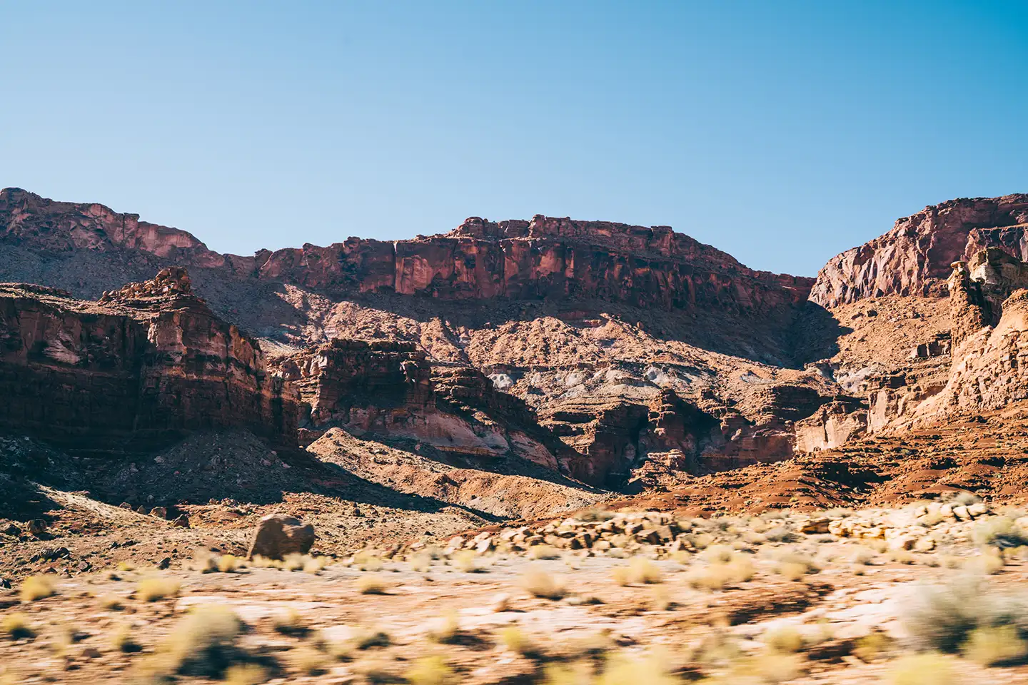Red and orange sandstone canyon walls rising above an arid desert floor under a clear blue sky in the American Southwest.