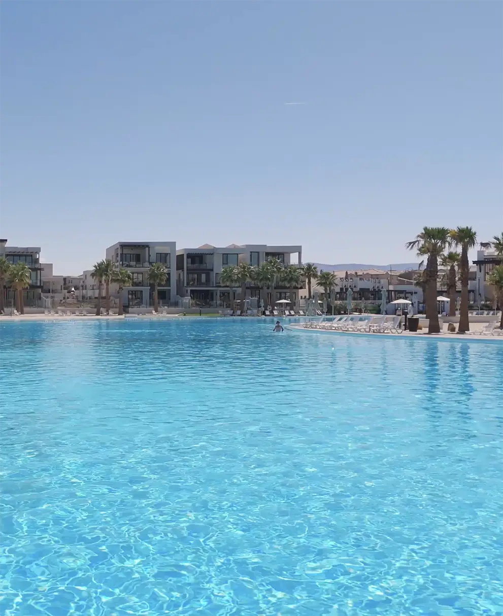 Crystal-clear turquoise lagoon pool with modern Desert Color residences and palm trees lining the waterfront in the background.