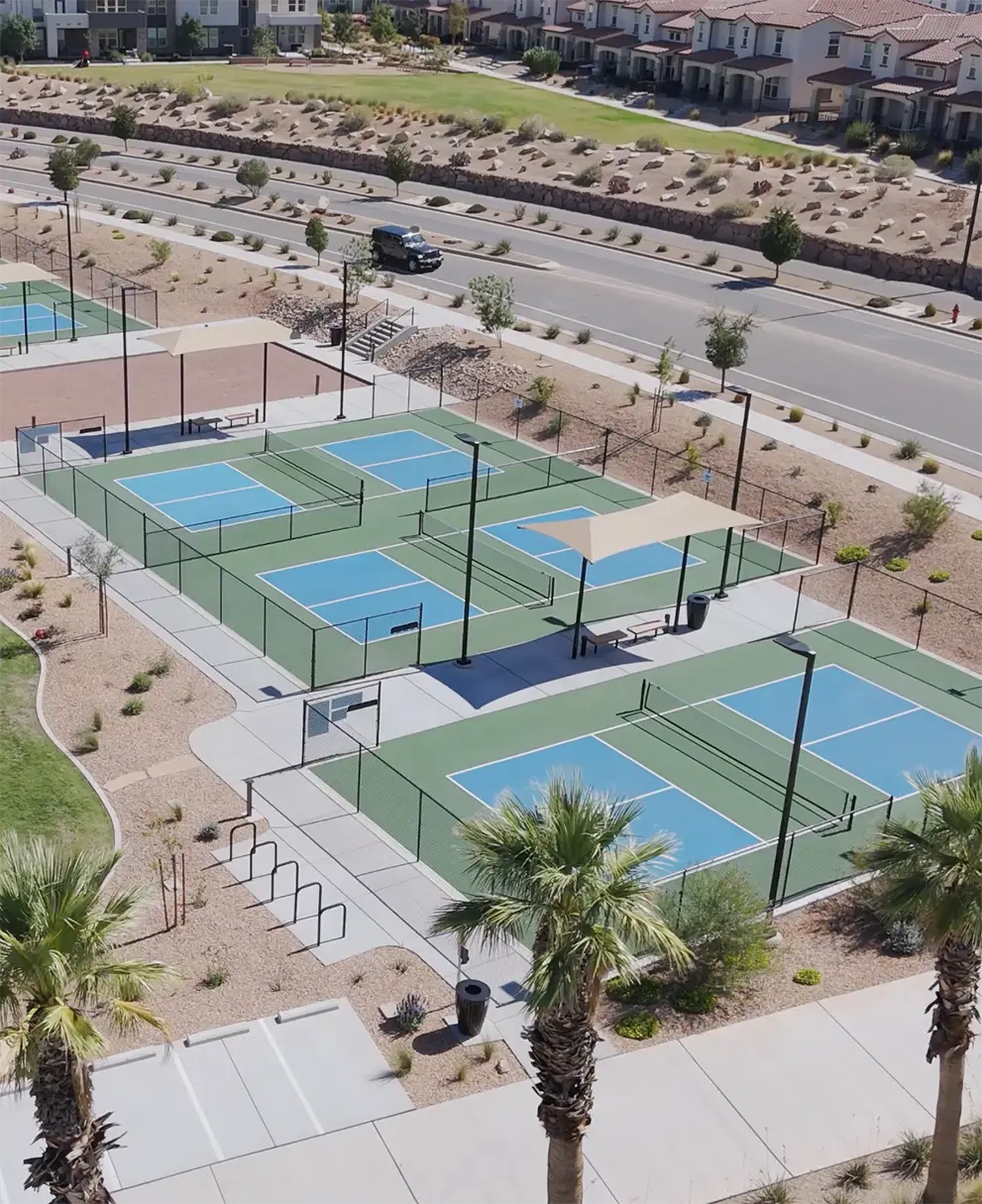 Aerial view of four pickleball courts with blue and green surfaces surrounded by palm trees and desert landscaping at Desert Color community.