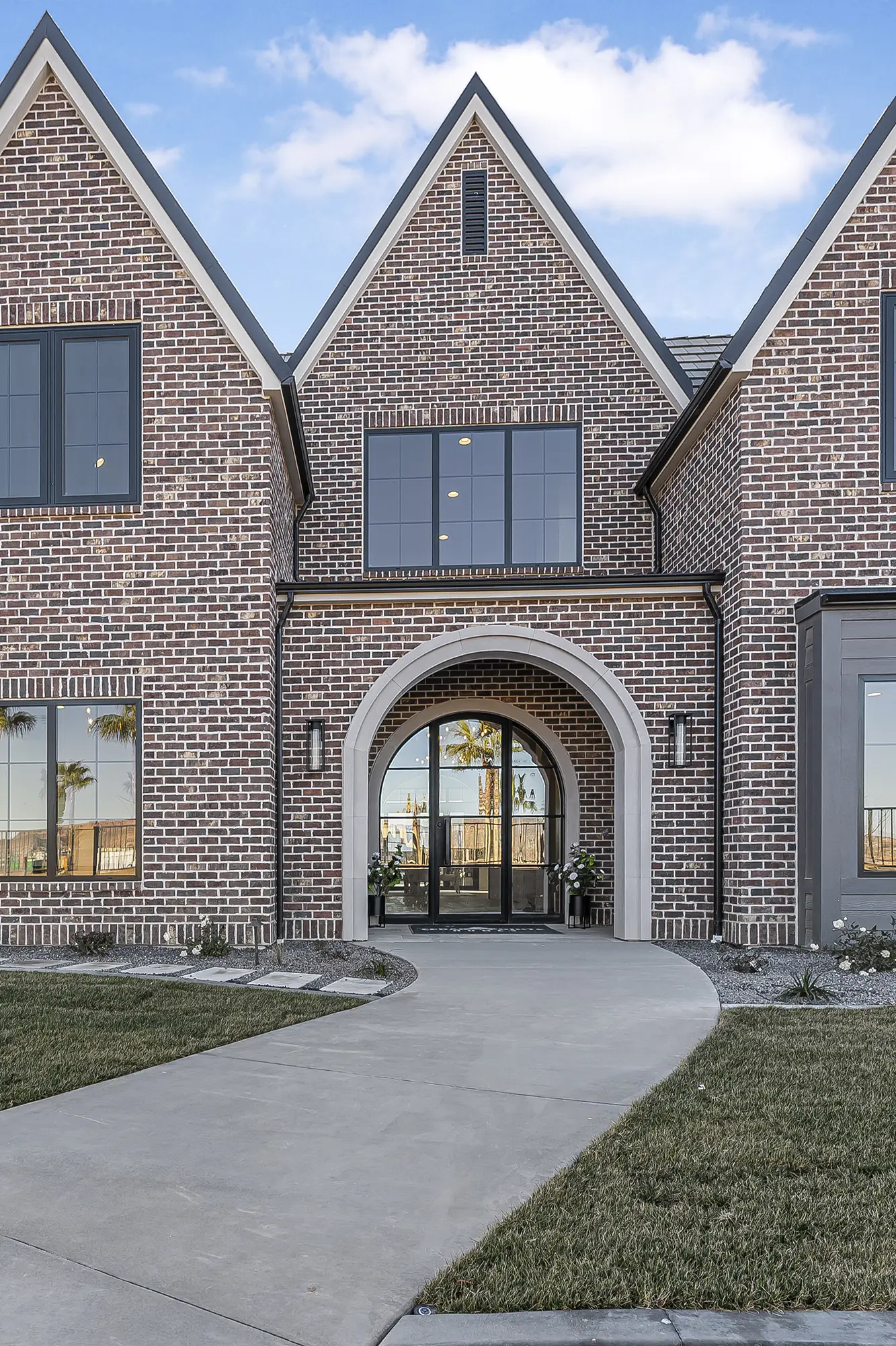 Villa Charmonte brick front entry with arched glass door, twin gables, and manicured walkway