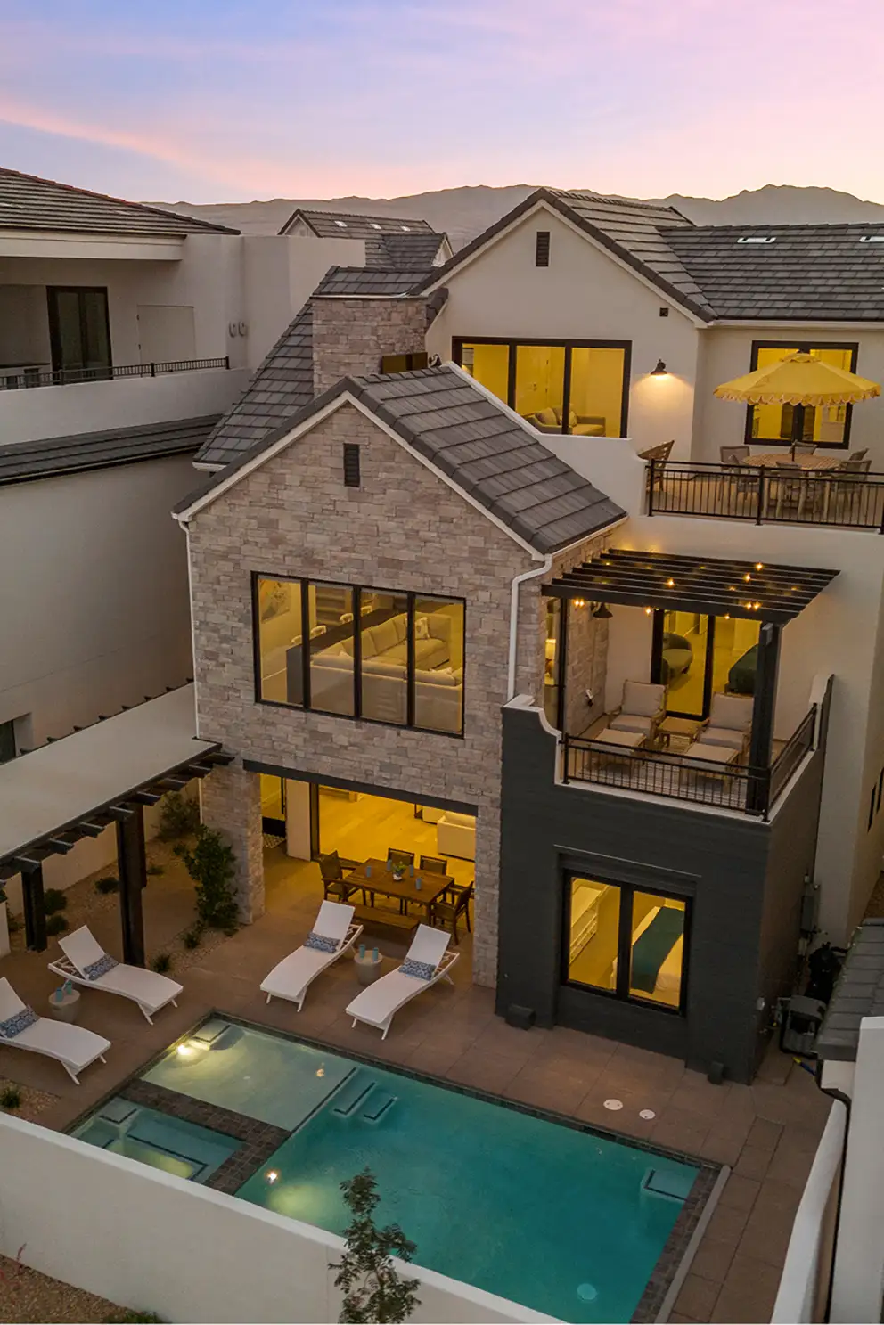 Aerial twilight view of Lula Cove courtyard with pool, spa, lounge chairs, and mountain backdrop