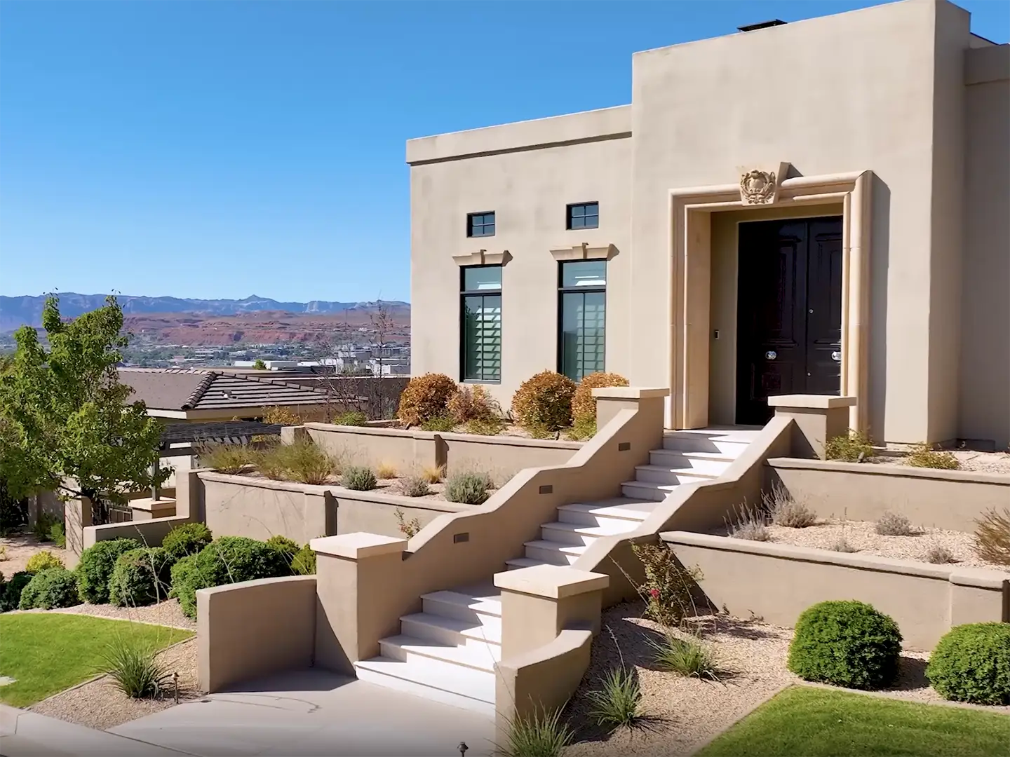 Stucco home entry with tiered staircase, terraced desert landscaping, and red rock views in a St. George hilltop community.