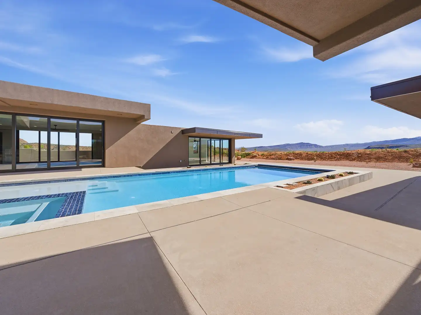 Courtyard pool and spa surrounded by stucco walls with sliding glass doors and open desert mountain views beyond.