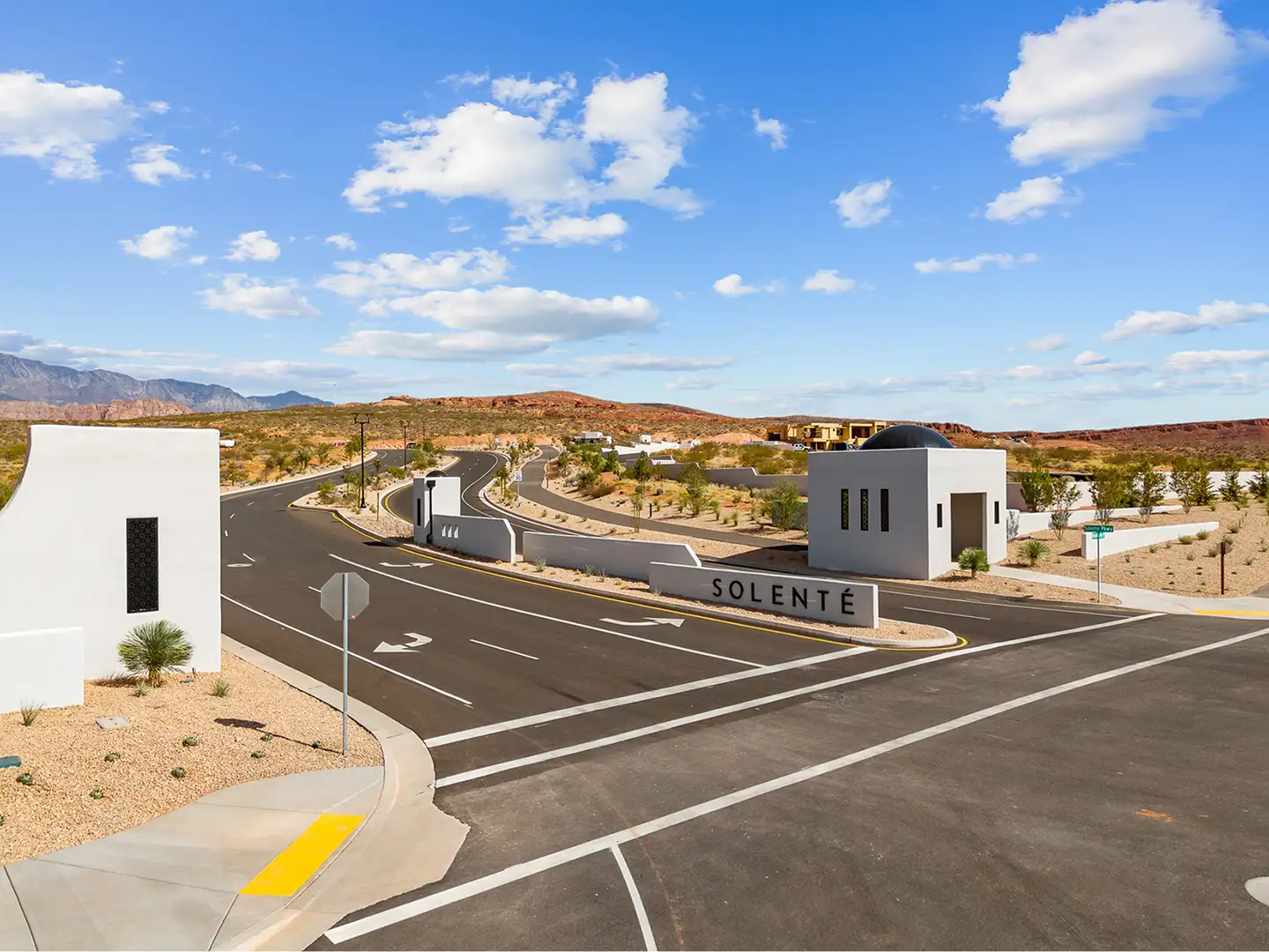 Aerial view of Solente community entrance road, monument signage, and modern gatehouse with red rock desert landscape beyond.