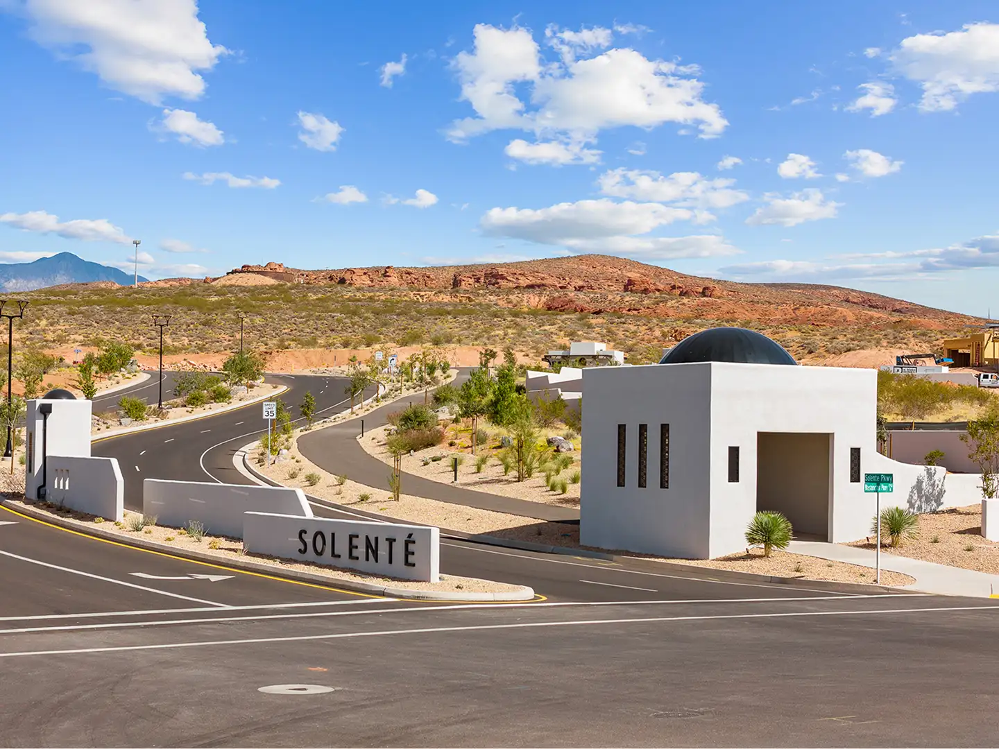 Solente community entrance with modern white gatehouse, monument sign, curved road, and red rock hills in Washington, Utah.