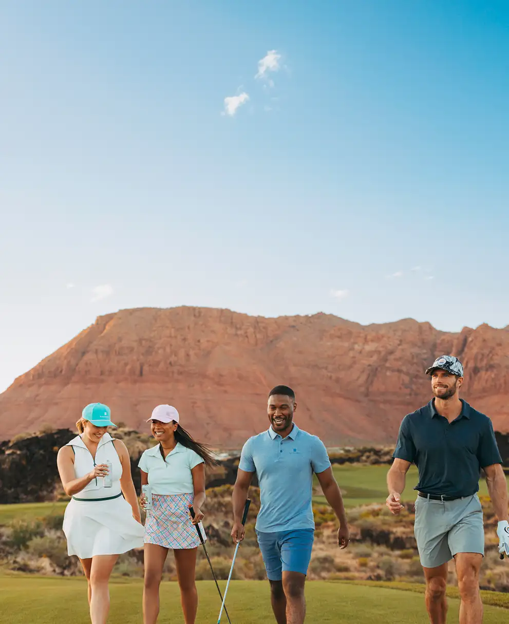 Four golfers walking together on a green fairway with a towering red rock mesa in the background
