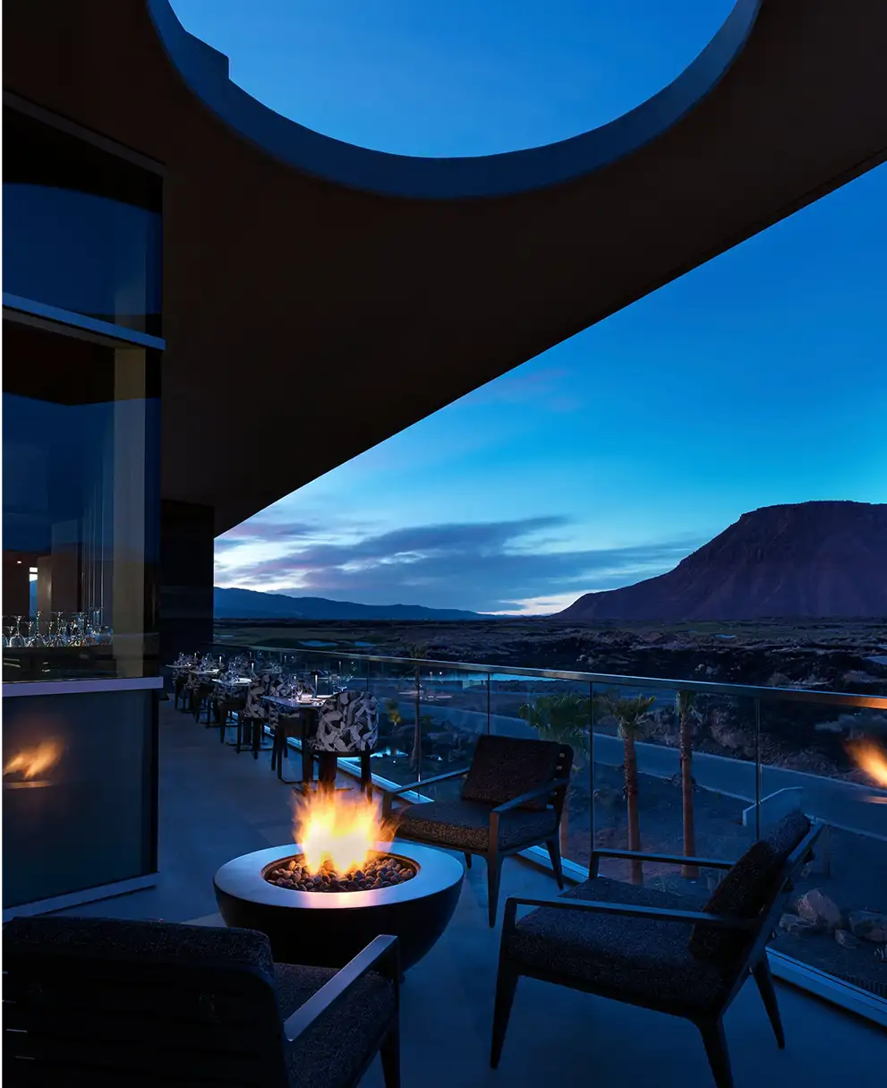 Outdoor terrace with glowing fire pit, lounge seating, and dining tables overlooking desert mountains at twilight
