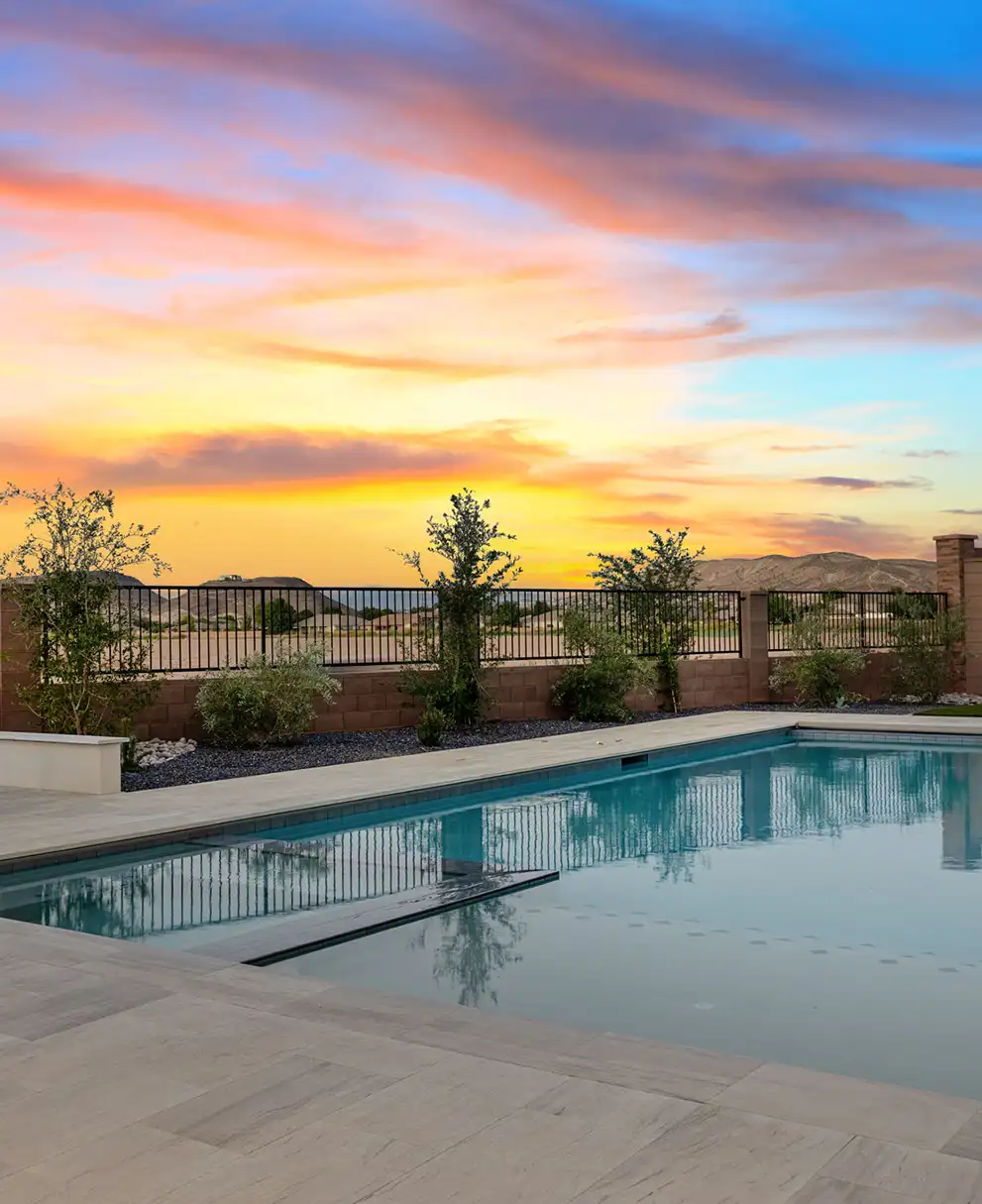 Backyard swimming pool reflecting a vibrant sunset sky with mountain views beyond a wrought-iron fence