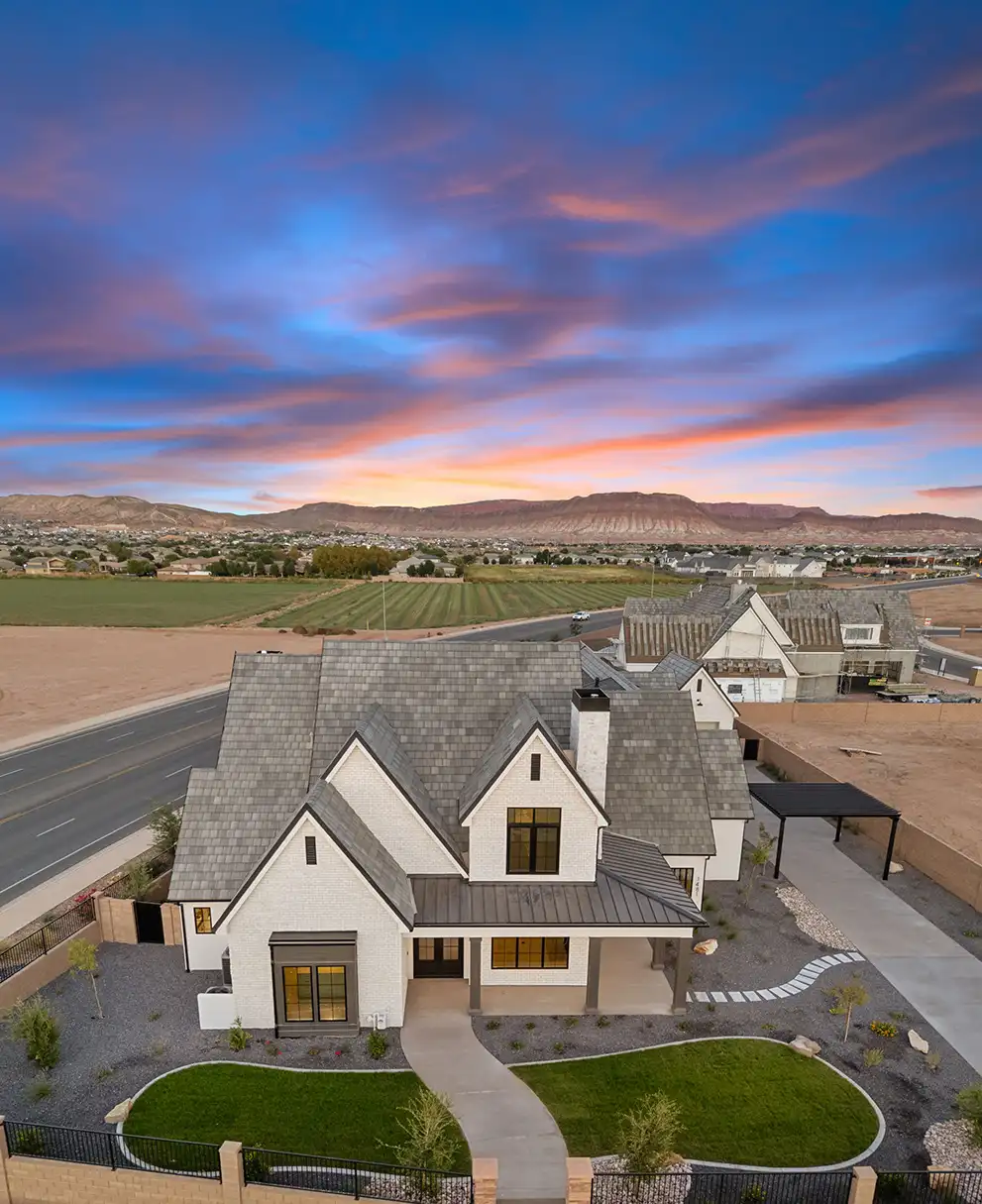 Aerial view of a white brick custom home with mountain views and a colorful sunset sky