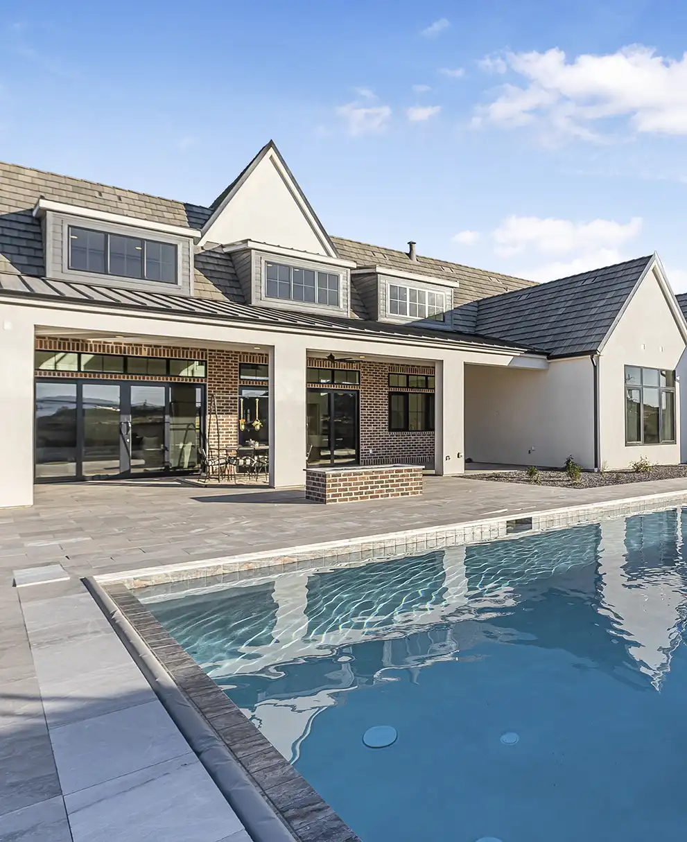 Custom home backyard featuring a rectangular pool, stone patio, and covered outdoor living area