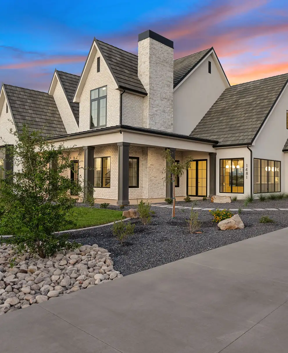 Modern farmhouse-style home with white brick, stone chimney, and black-framed windows at twilight