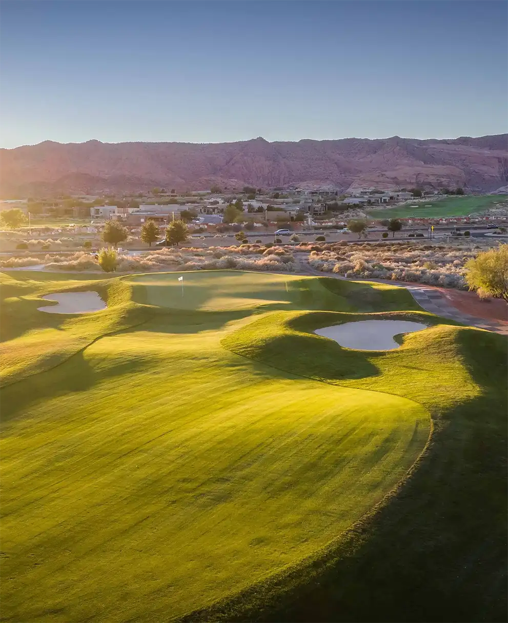 Lush green golf course at golden hour with red rock mountains in the background