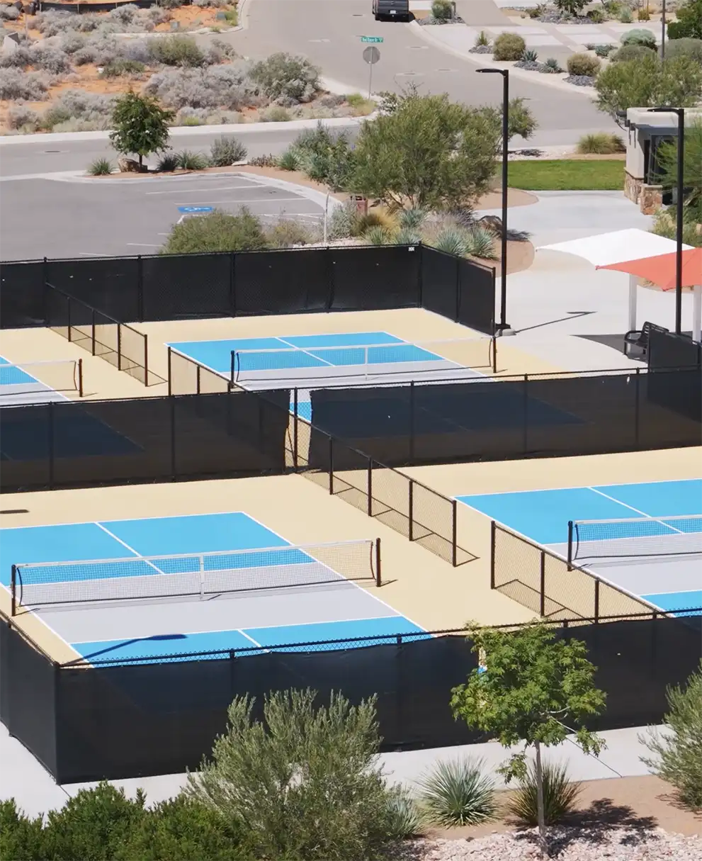Aerial view of four blue pickleball courts surrounded by desert landscaping at a residential community