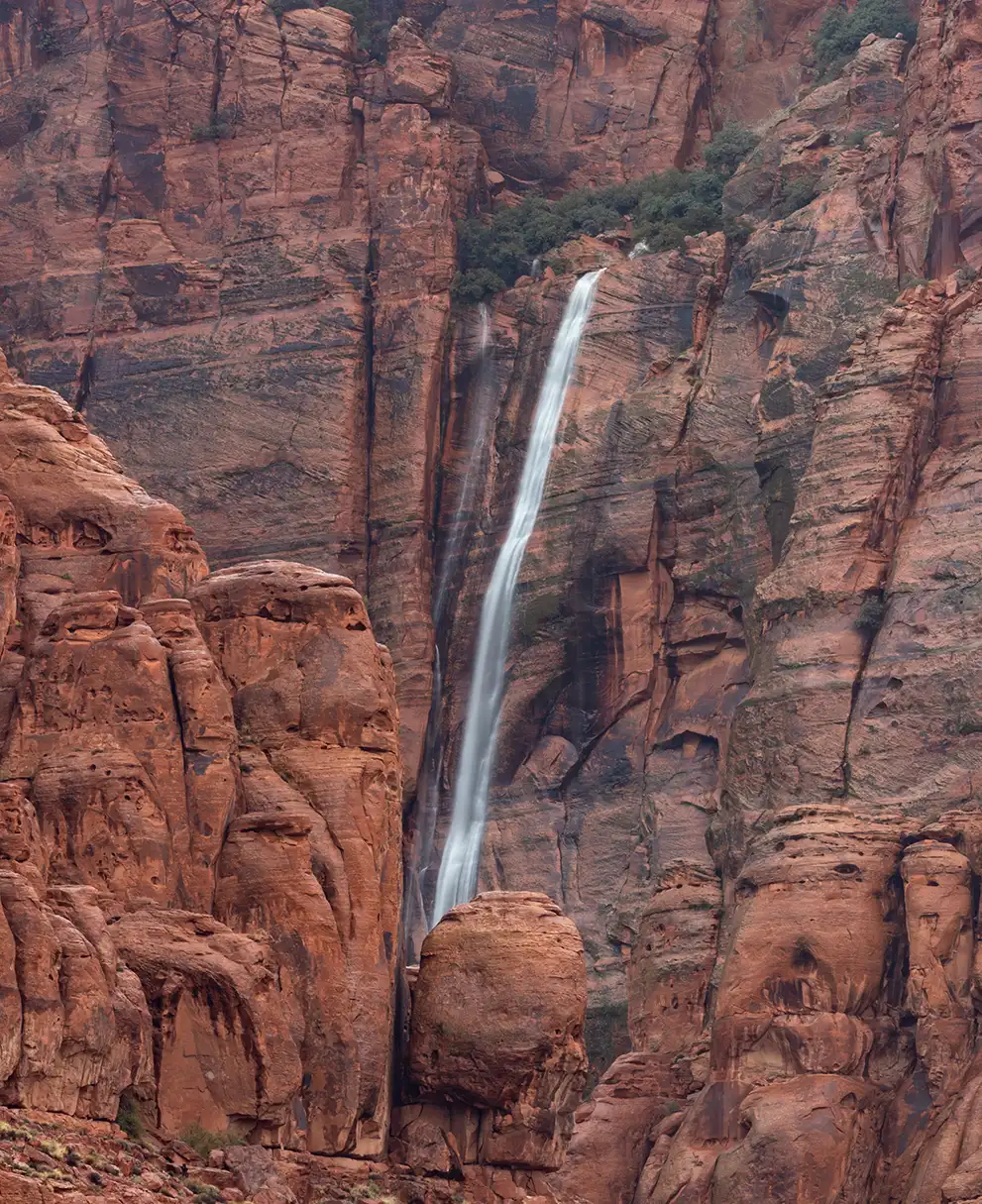 Tall waterfall streaming down sheer red sandstone cliff walls in a narrow canyon