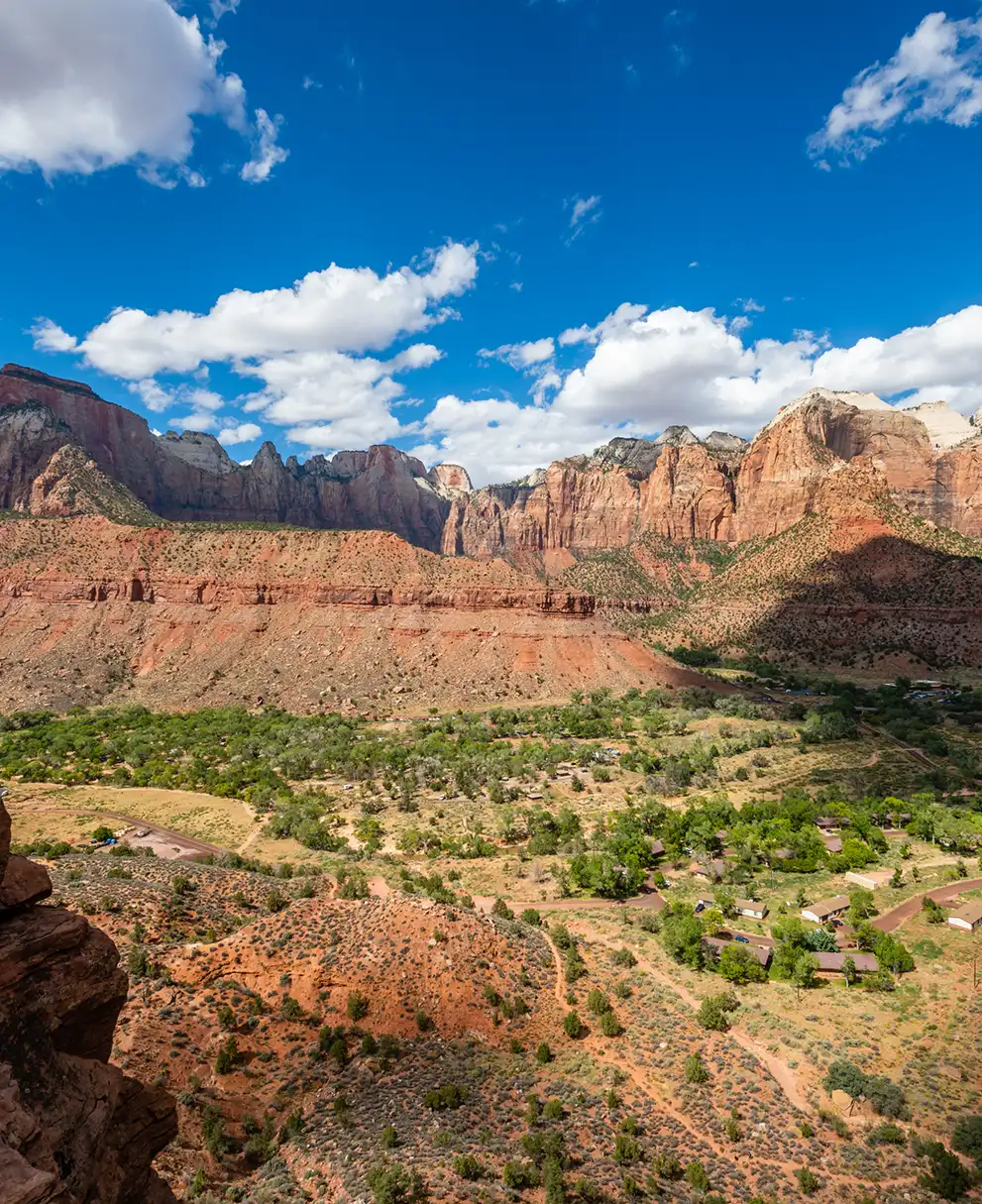 Panoramic overlook of a red rock canyon valley with towering sandstone cliffs and lush green vegetation below