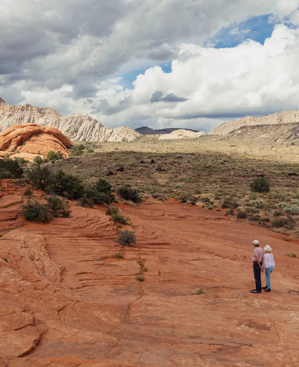 Couple standing on red sandstone slickrock enjoying views of layered white and orange rock formations