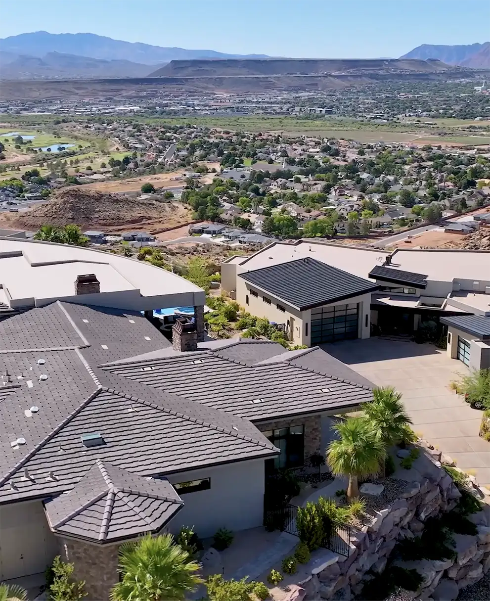 Aerial view of luxury hillside homes with dark rooftops overlooking a sprawling desert valley and distant mountains