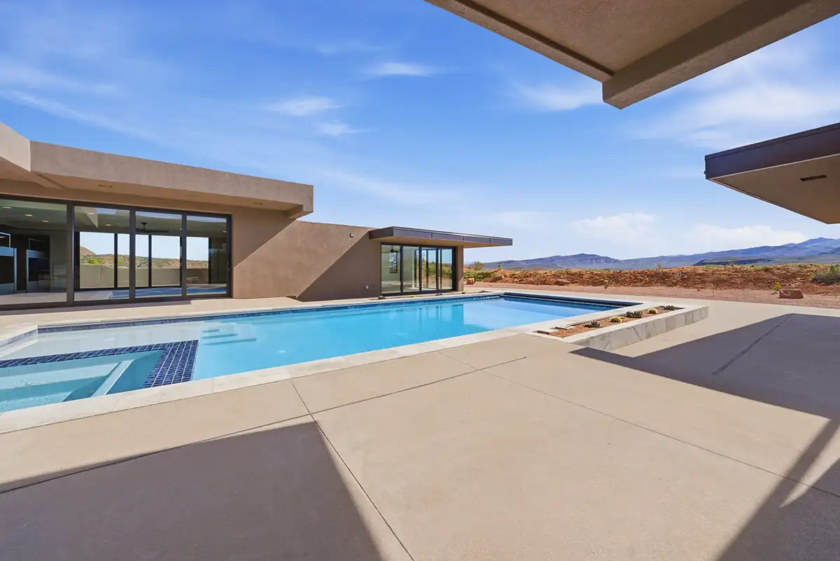 Modern desert home patio featuring a blue swimming pool and spa surrounded by concrete decking with mountain views on the horizon.