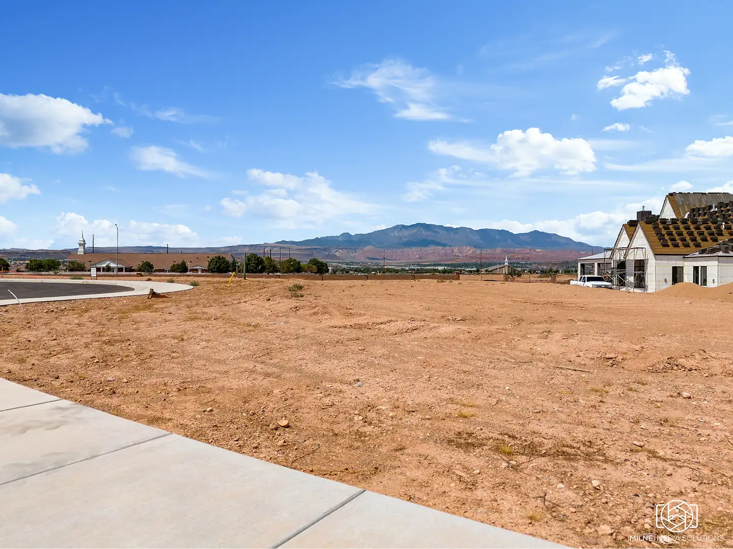 Ground-level view of a prepared home lot with panoramic mountain views and a home under construction next door