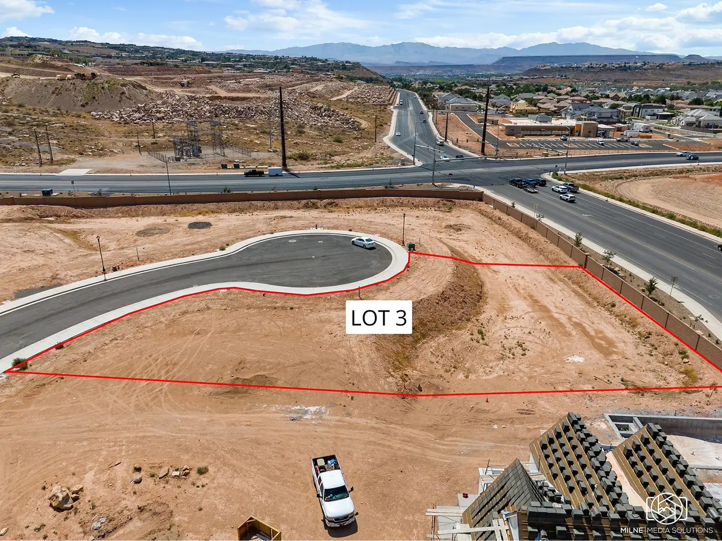 Aerial view of a home lot looking west toward a main road, desert hills, and distant mountain ranges