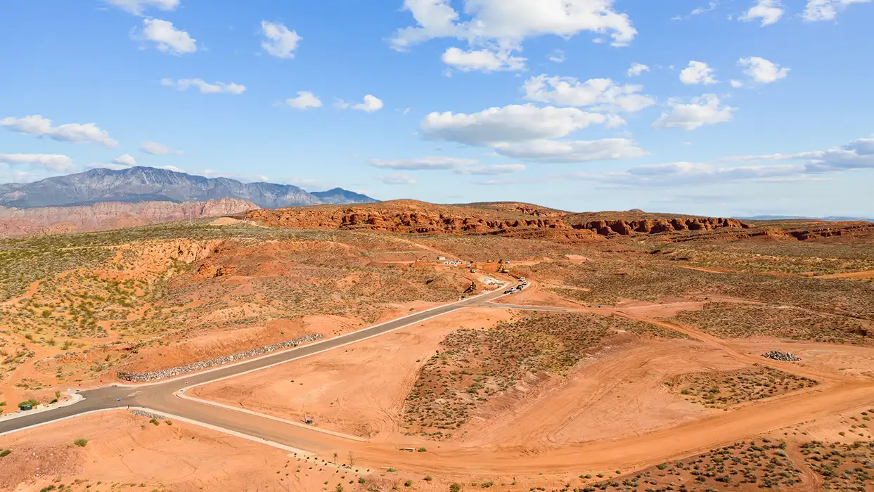 Aerial view of prepared home lots on red desert terrain with red rock cliffs and mountain range in the background
