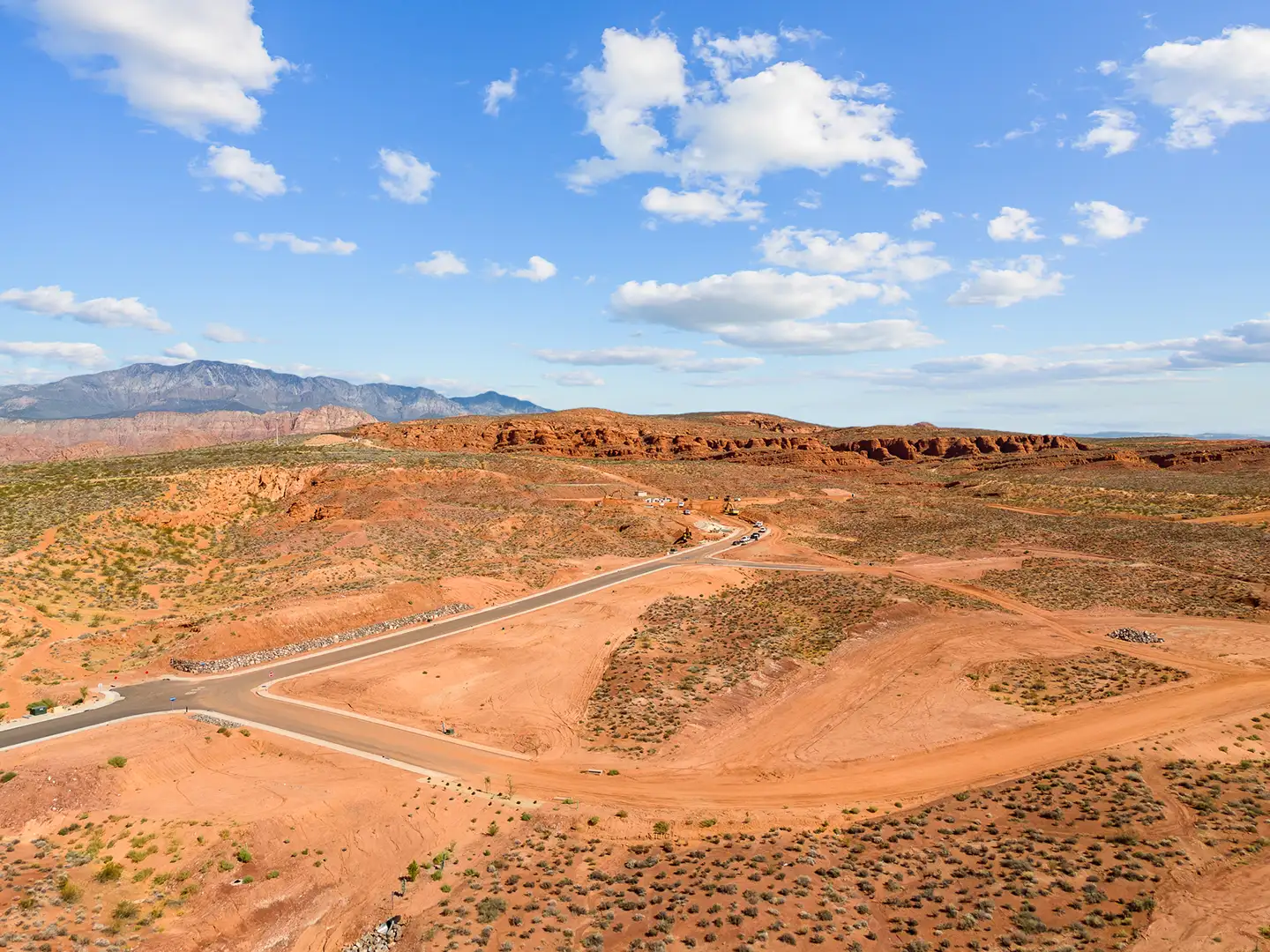 Aerial drone view of a new residential development with paved roads curving through red desert landscape near sandstone cliffs