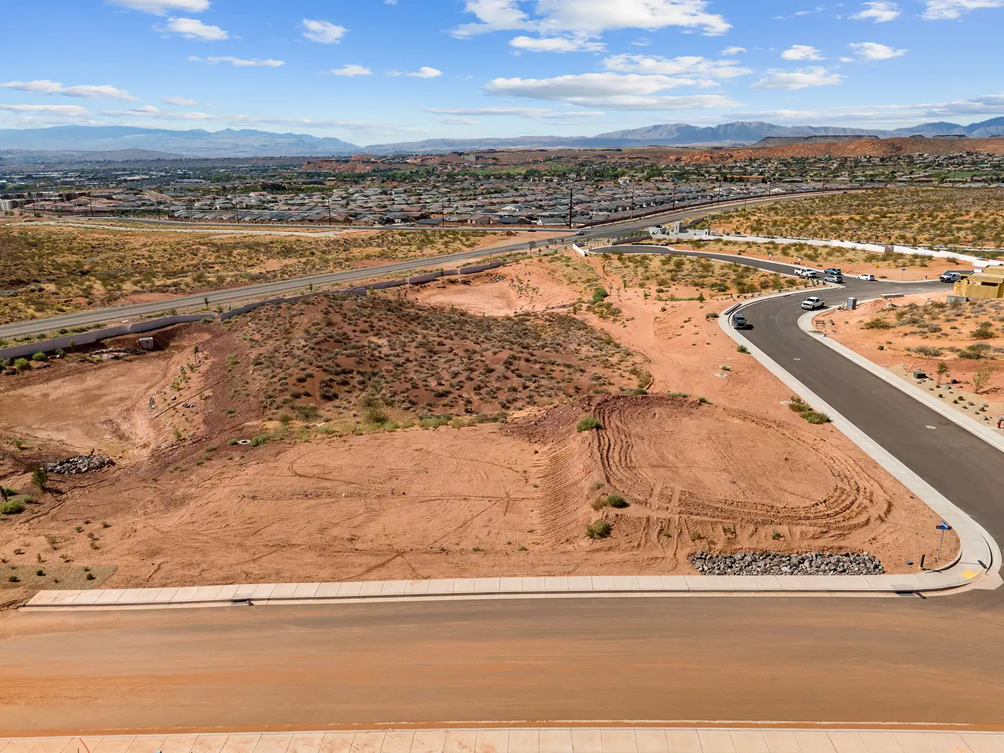 Aerial view of corner home lots near a highway interchange with a sprawling desert community and mountains in the distance