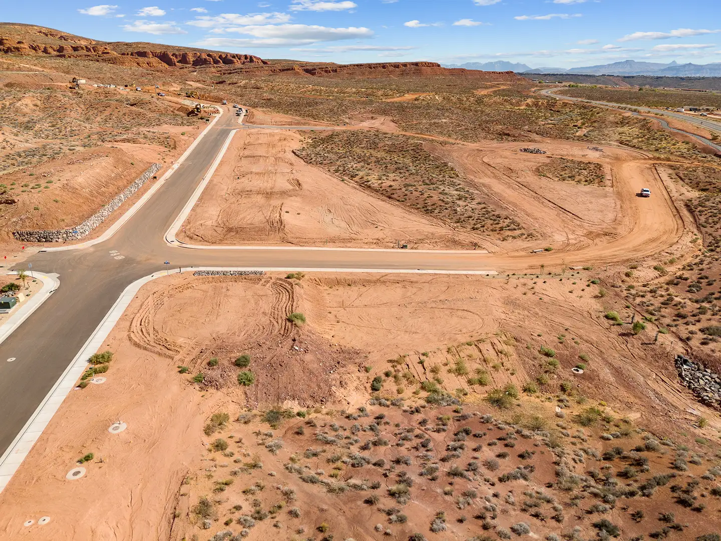 Aerial view of graded home lots with paved streets surrounded by red rock formations and desert brush