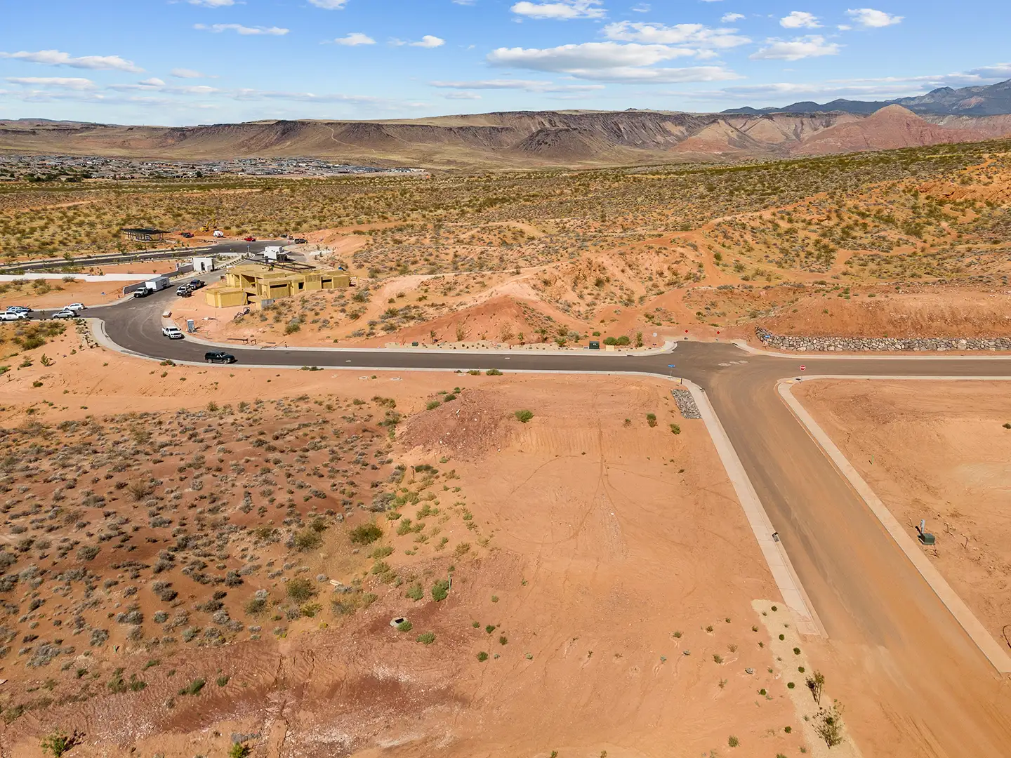 Aerial view of a developing residential community with new roads, homes under construction, and a desert town in the valley below