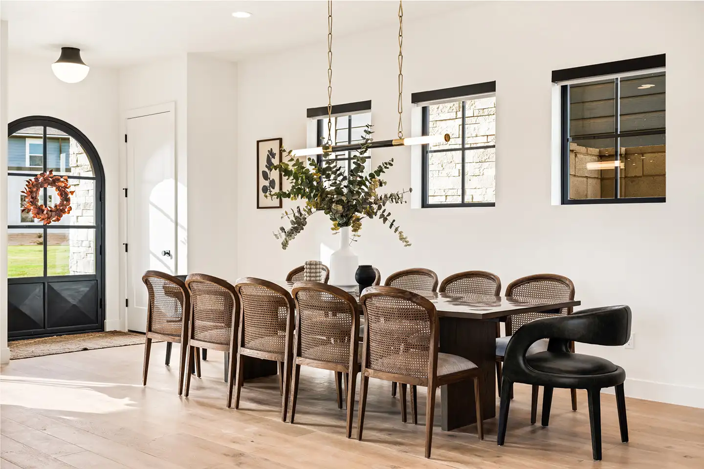 Designer-styled dining room with long wood table, cane-back chairs, modern pendant light, and arched front entry.