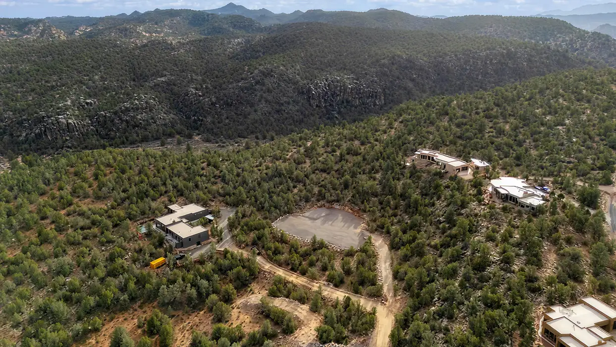 Aerial view of custom homes on a cul-de-sac surrounded by pinyon-juniper forest with rugged mountain ridges in the background.
