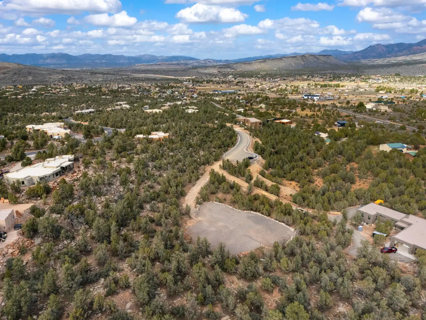 Aerial drone view of a cleared homesite in a high-desert community with scattered houses and distant mountain ranges.