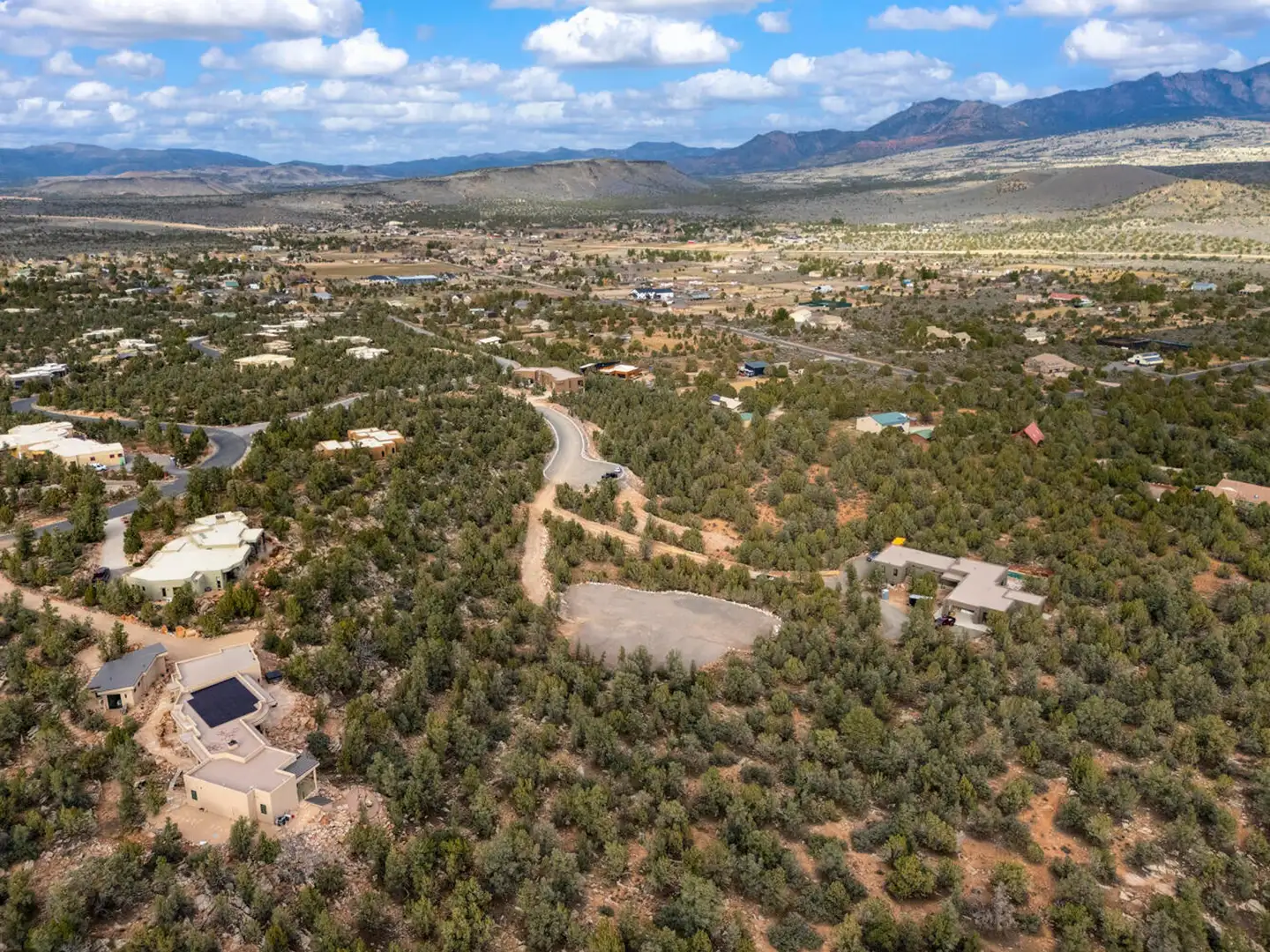 Aerial view of a cleared building lot among houses, juniper-covered hills and distant blue mountain ridges.