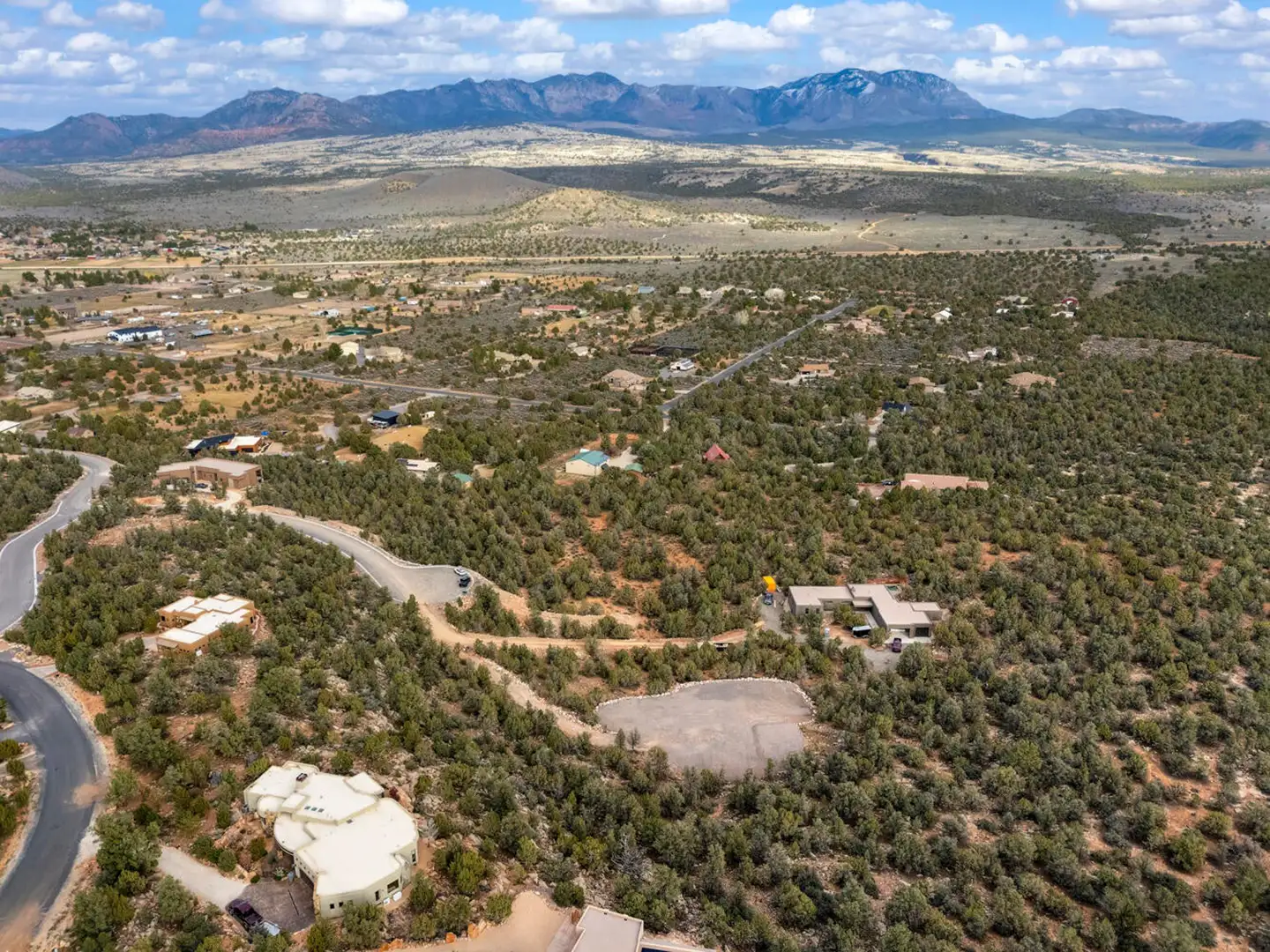 Aerial of a cleared homesite in a desert neighborhood with red-rock mountain ridges along the horizon.