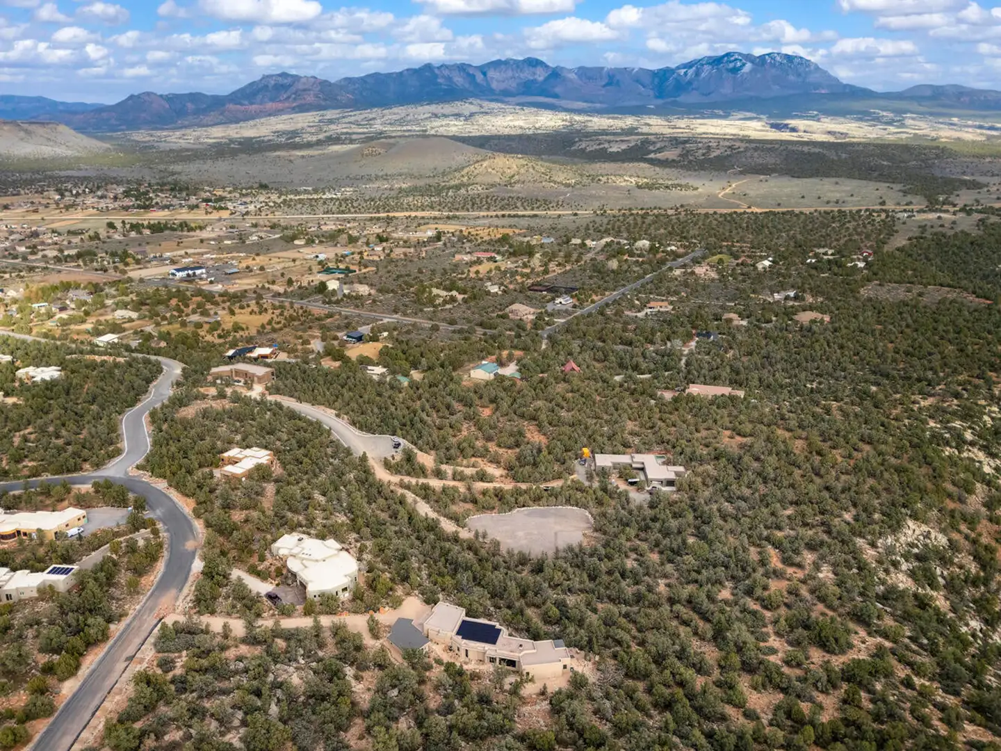 Aerial view of a high-desert residential community with winding streets, scattered homes and a distant mountain backdrop.