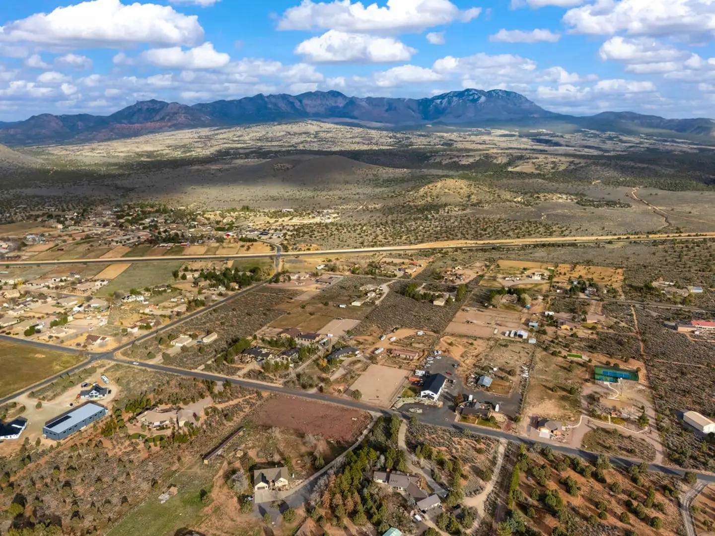 Aerial of a valley neighborhood with rural homes, fields and a sweeping red-rock mountain range in the background.