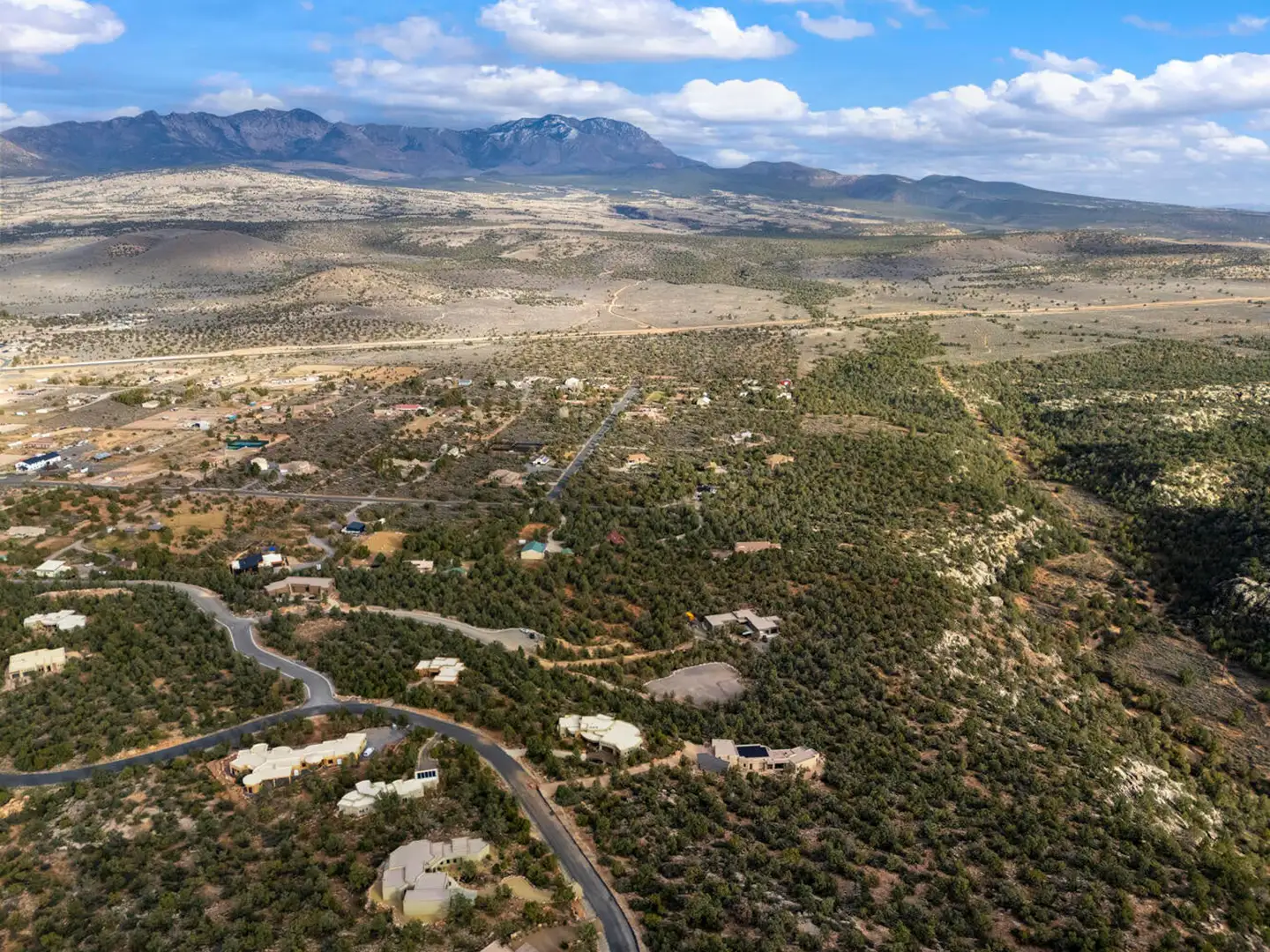 Aerial view of a high-desert neighborhood with scattered homes, winding roads and a long mountain range on the horizon.