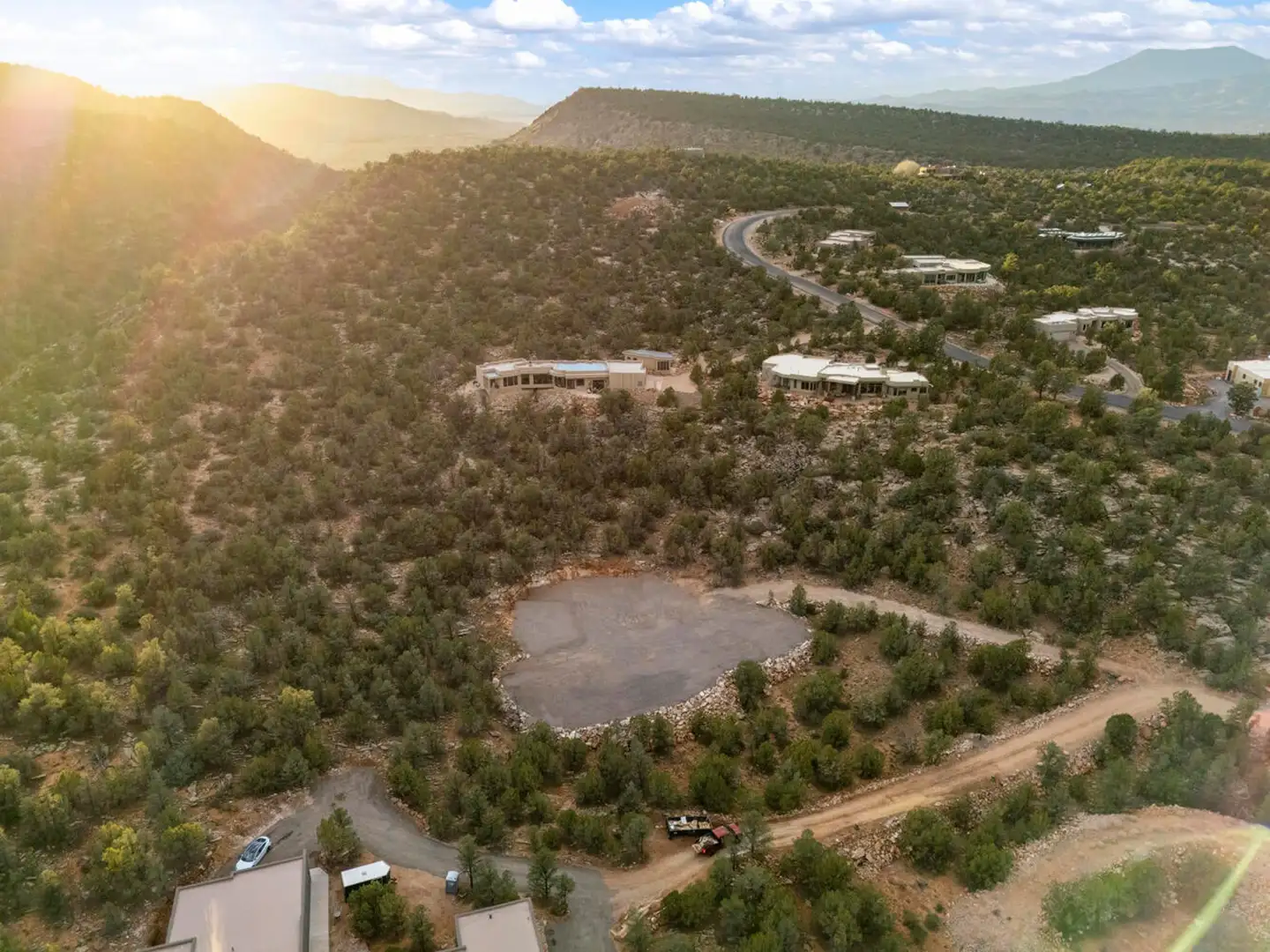 Aerial sunset view of a cleared homesite ringed by upscale homes, juniper hills and distant mountain ridges.